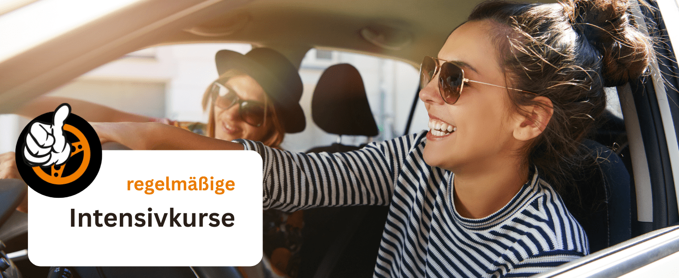 Two women in a car smiling; a white sign with orange text reads 'regelmäßige Intensivkurse' promoting regular intensive courses.